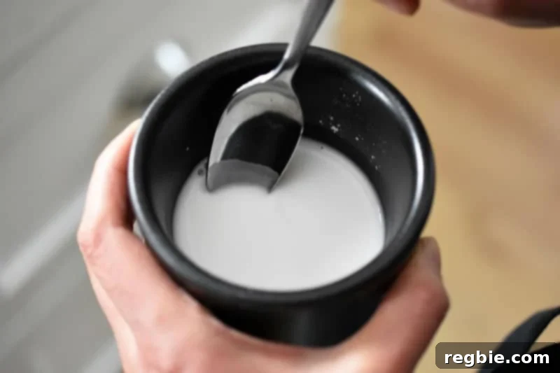 An overhead shot of a small black ramekin holding a smooth, white arrowroot slurry, ready to thicken the gravy.