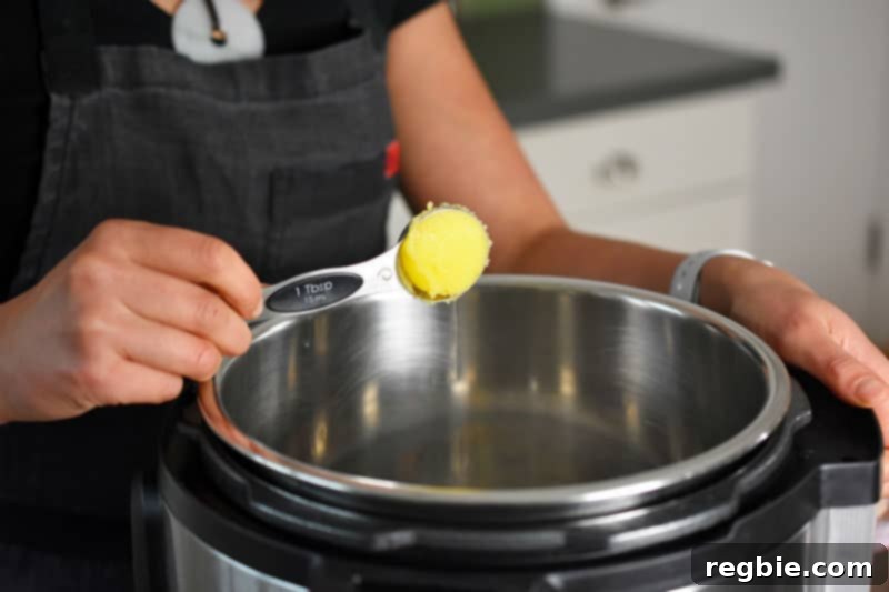 A hand adding a tablespoon of golden ghee into an open Instant Pot, ready for sautéing.