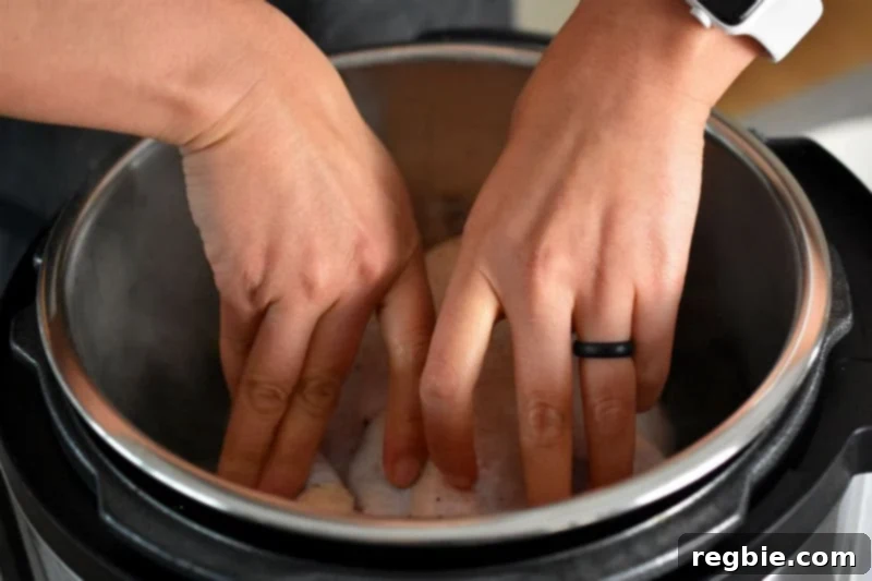 Two hands gently pressing a whole chicken breast-side down into an open Instant Pot, initiating the searing process.