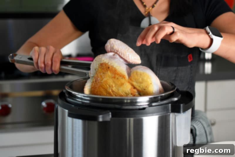A person using tongs to carefully turn a whole chicken in the Instant Pot, revealing its beautifully browned underside.