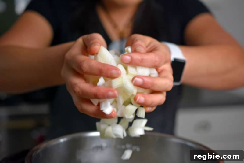Two hands adding freshly chopped onions to the Instant Pot, ready to sauté and create the gravy's aromatic base.