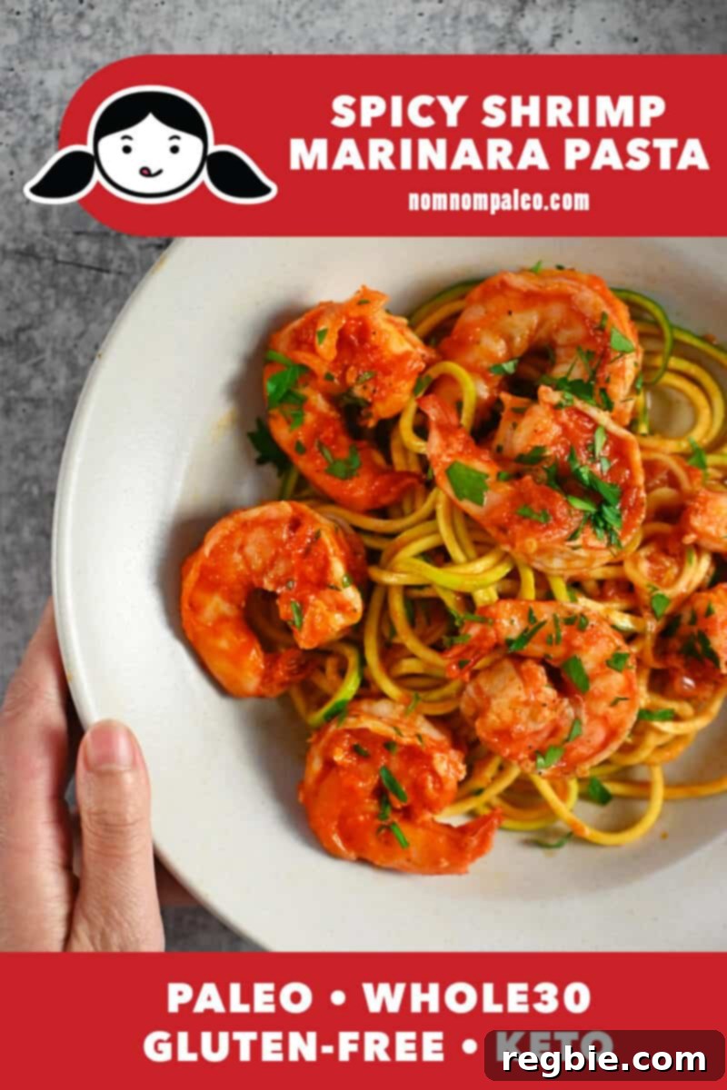 An overhead shot of a hand holding a bowl filled with Whole30 and keto spicy shrimp pasta with marinara sauce on zucchini noodles, garnished with fresh parsley.
