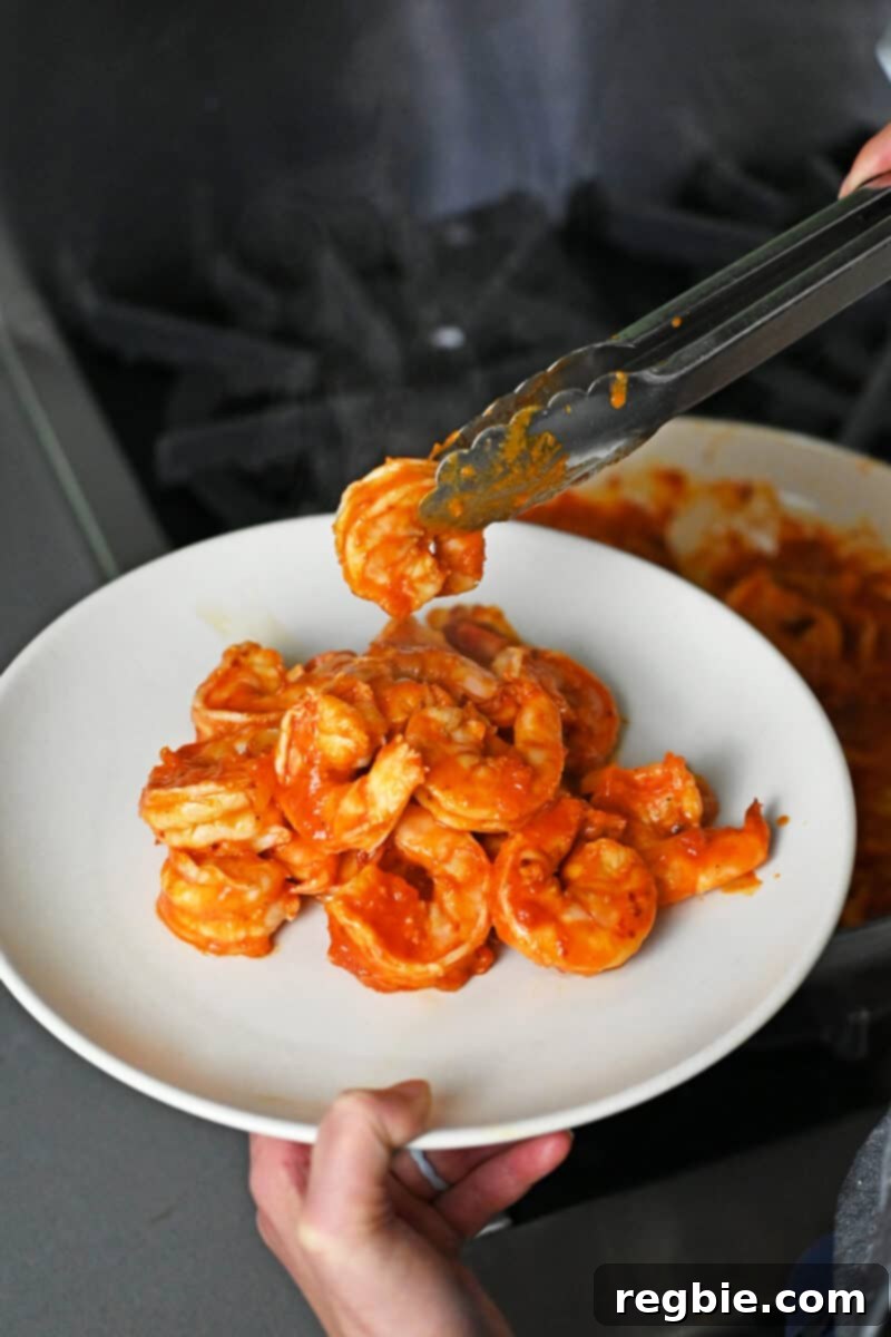 Using tongs to transfer cooked spicy shrimp to a platter, ready to be reunited with the zoodles.