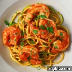 An overhead shot of a shallow bowl filled with Whole30, paleo, and keto spicy shrimp pasta with marinara sauce and zucchini noodles, garnished with fresh parsley.
