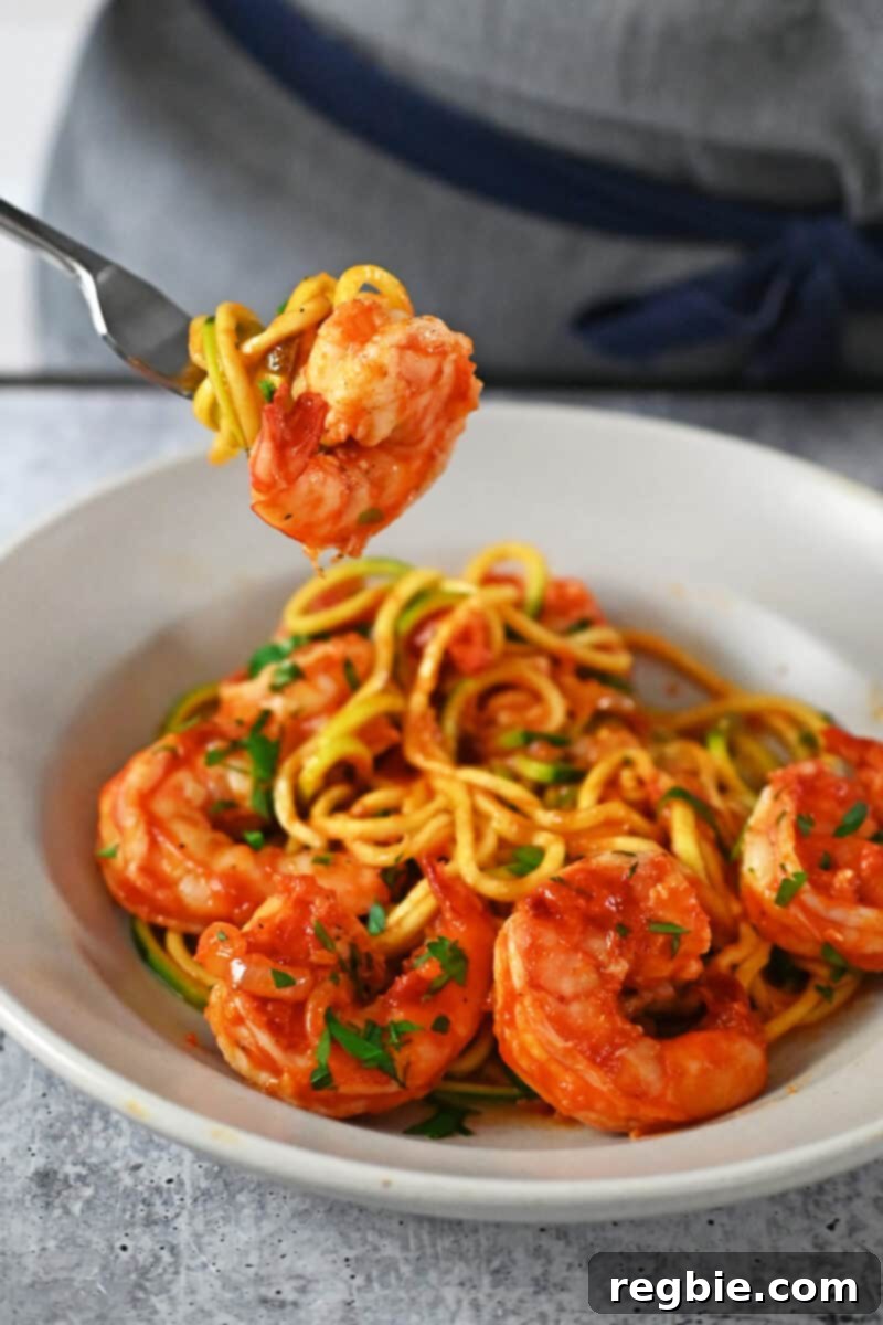 A fork taking a bite of spicy shrimp pasta with zucchini noodles, highlighting the texture and freshness of the dish.