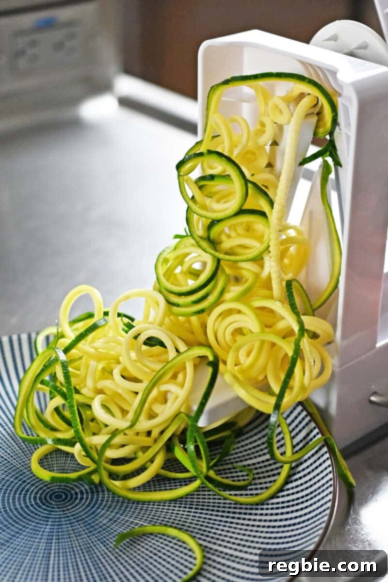 A spiralizer is making zucchini noodles, showcasing the fresh, green strands being formed.
