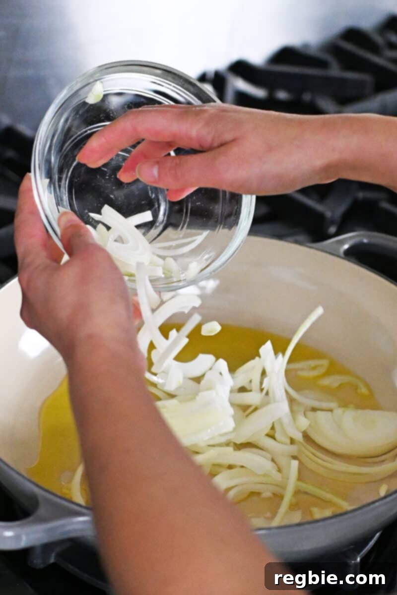 Adding thinly sliced onions to a large skillet with hot oil, beginning the sautéing process.