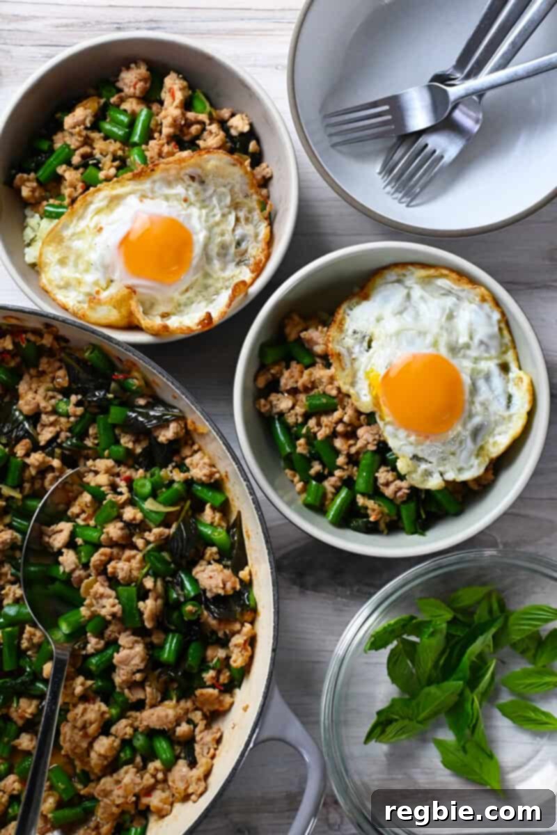 A skillet filled with Thai Basil Chicken is next to two bowls of it topped with fried eggs