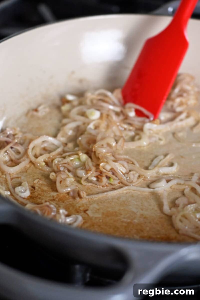 Sauteing sliced shallots in a large cast iron skillet for Thai Basil chicken