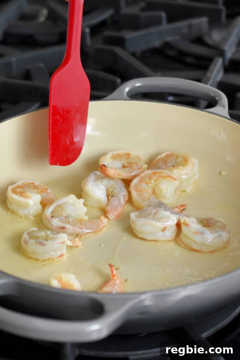 Succulent shrimp being expertly sautéed in an enameled cast iron skillet, developing a beautiful pink hue.