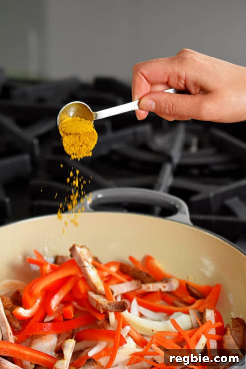 Someone adding a spoonful of fragrant curry powder to a skillet filled with colorful matchstick vegetables, shrimp, and Char Siu.