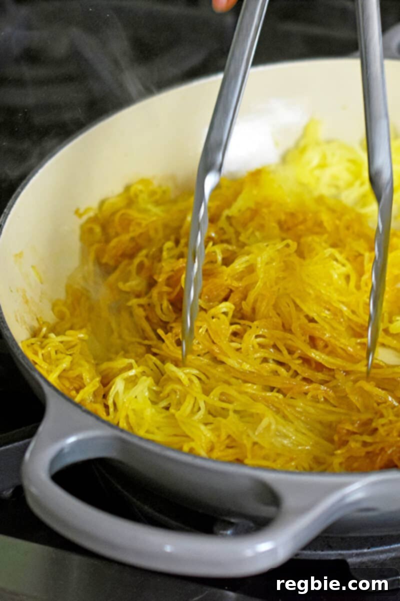 A pair of metal tongs gracefully stirring spaghetti squash in an enameled cast iron skillet, ensuring even sauce distribution.
