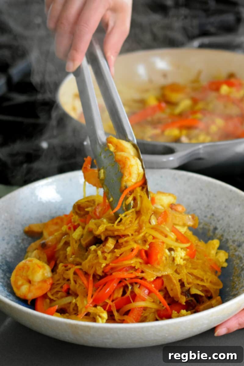 A pair of tongs delicately adding a succulent shrimp to a beautifully arranged bowl of paleo and Whole30 Singapore Noodles.