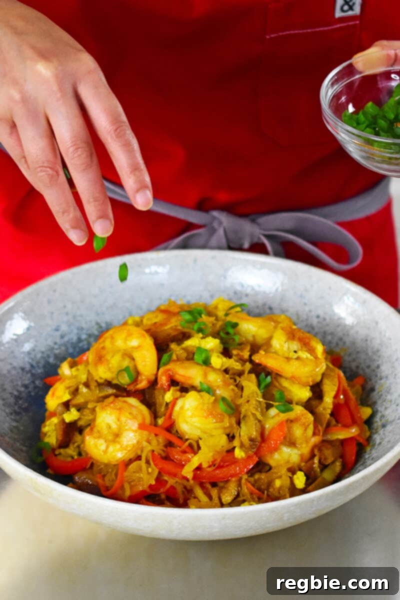 Adding fresh, thinly sliced scallions as a vibrant garnish to a delicious bowl of paleo and Whole30 Singapore noodles.