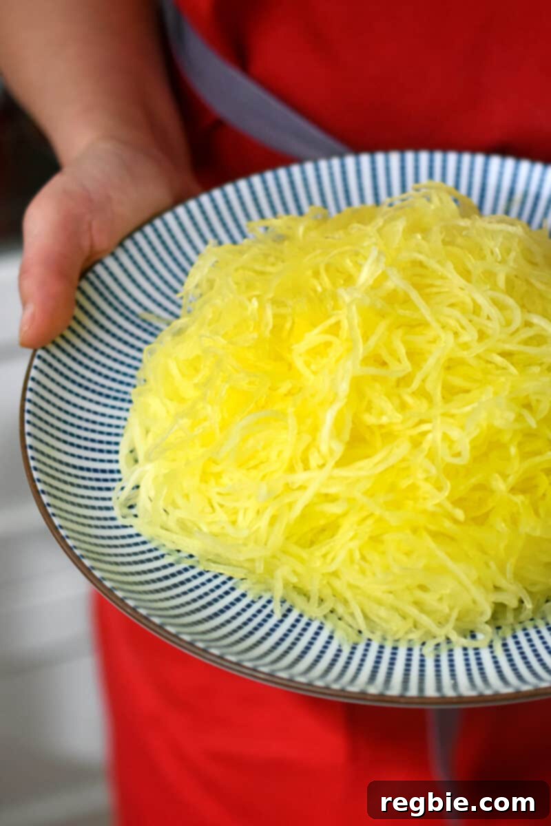 A hand is holding a blue plate with cooked and shredded spaghetti squash, ready to be transformed into delicious noodles.