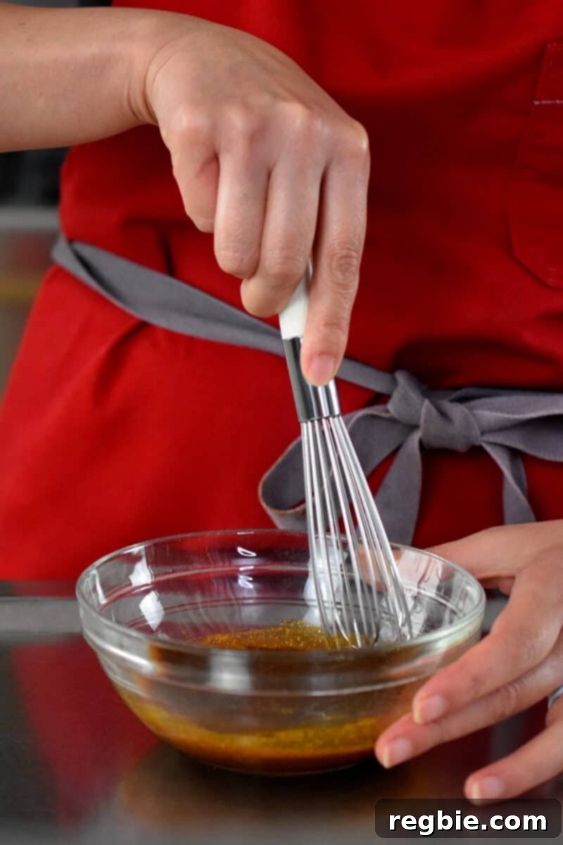 A person in a red apron is expertly whisking the vibrant sauce for Singapore noodles in a small clear bowl.