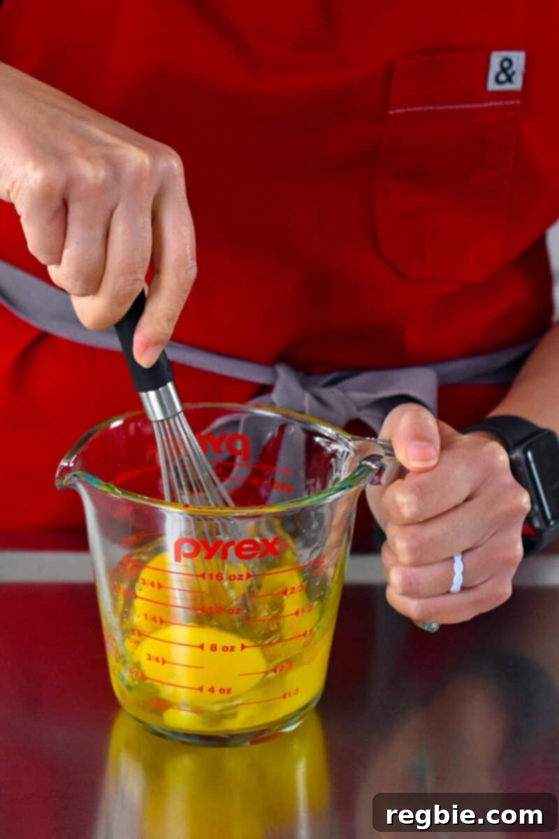 Whisking raw eggs in a clear liquid measuring cup, a crucial step for fluffy scrambled eggs.