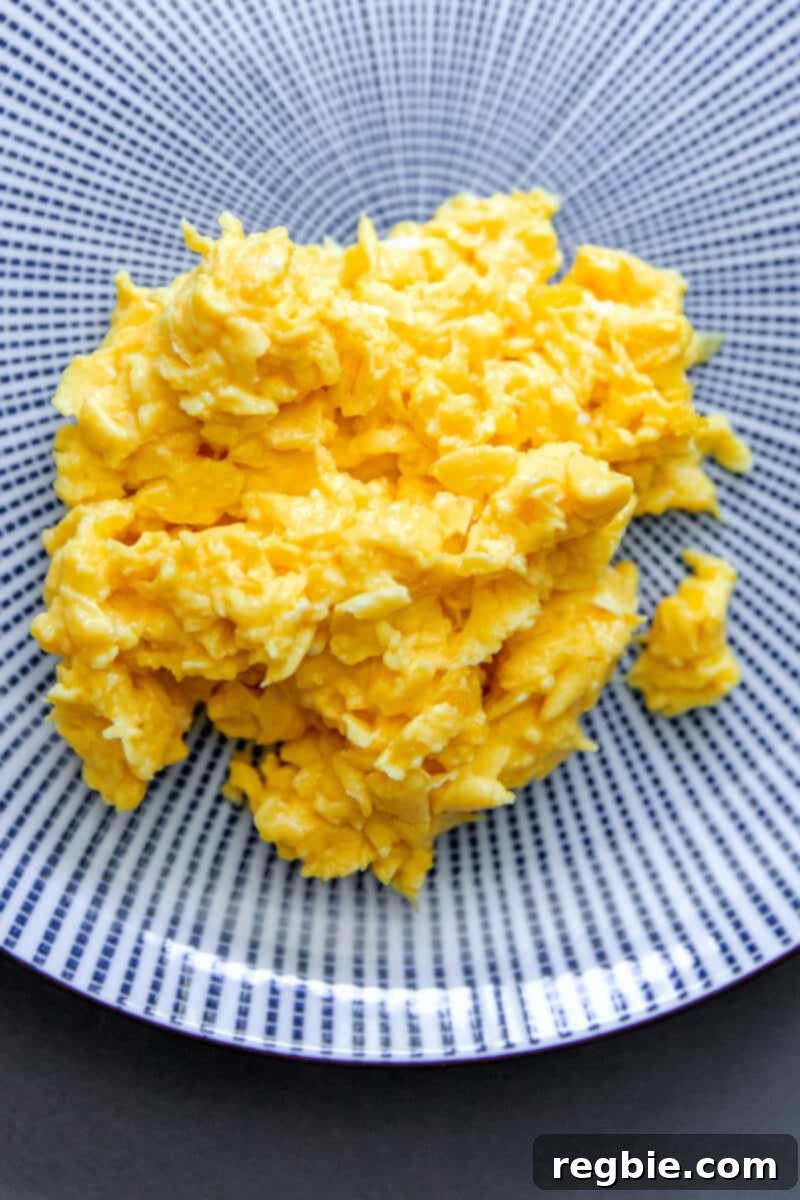 An overhead shot of a blue and white plate topped with fluffy scrambled eggs, perfectly cooked and ready to be added to the dish.