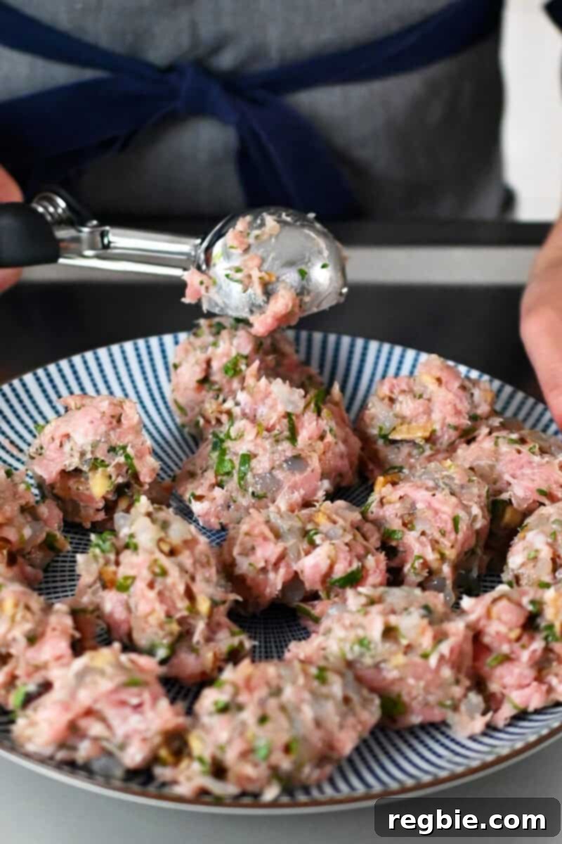 A medium ice cream scoop is used to portion out wonton meatballs on a blue and white plate for consistency.