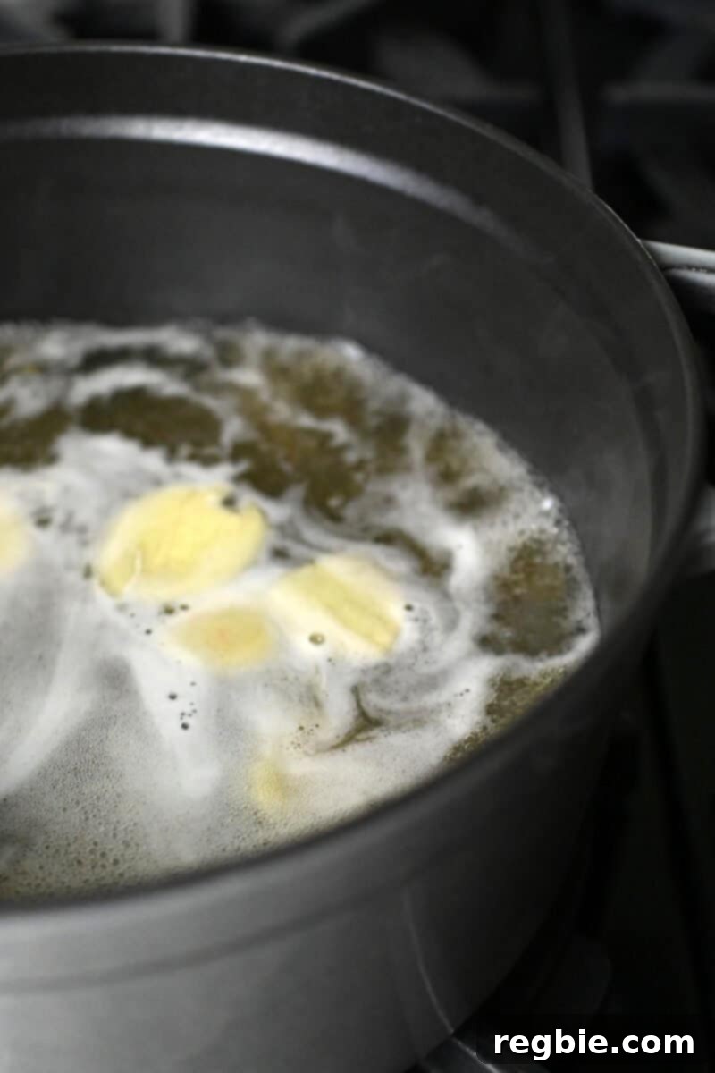 Chicken broth with ginger slices is simmering in a large pot, creating an aromatic base.