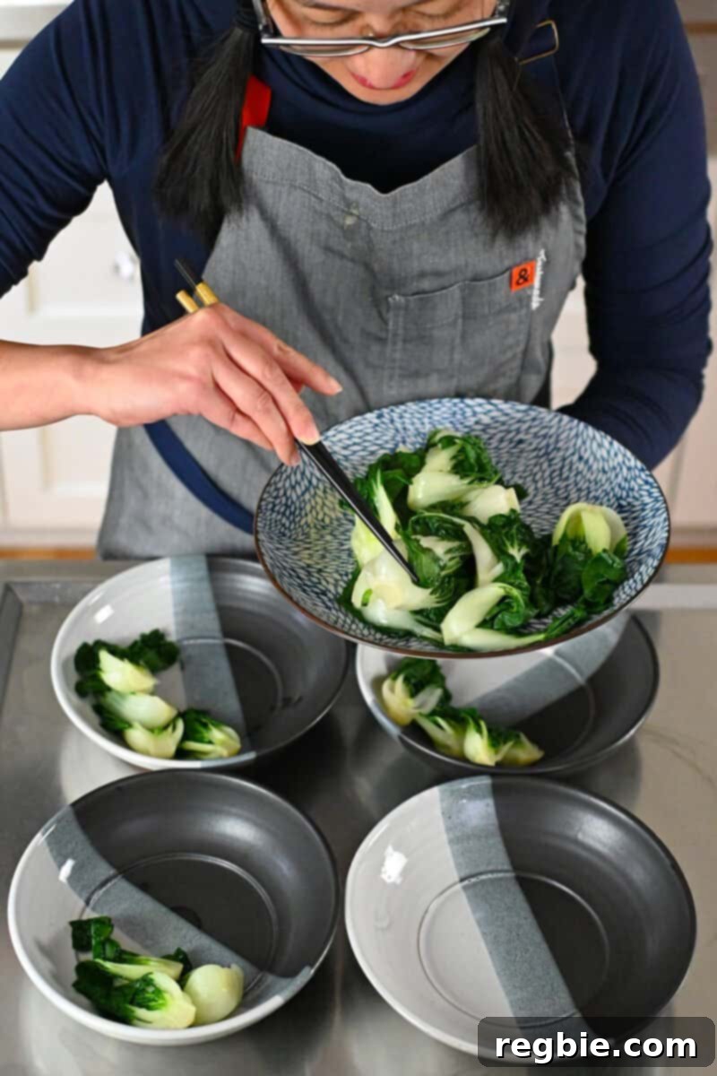A woman is dividing cooked baby Bok Choy into four soup bowls, preparing for serving.