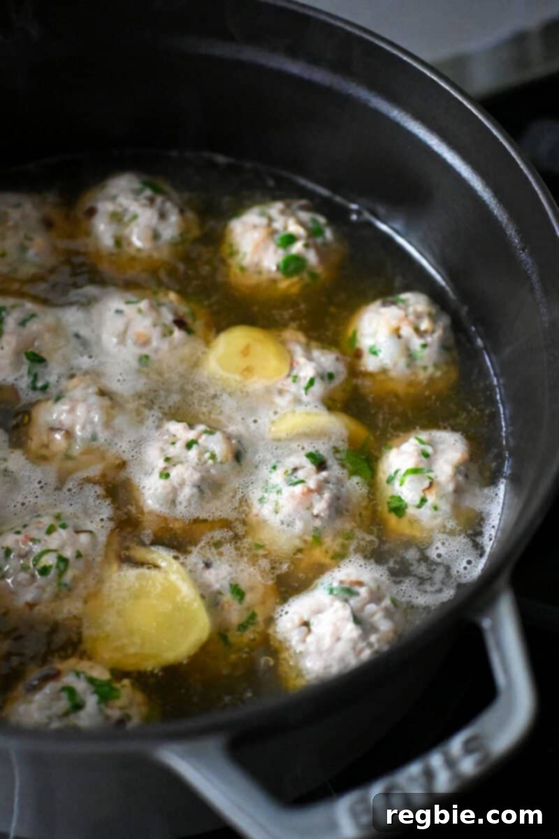 Wonton Meatballs simmering gently in a gingery chicken broth in a large pot, cooking to perfection.