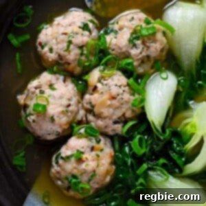 An overhead shot of a bowl with wonton meatballs and baby Bok Choy in a bowl of clear broth, garnished with fresh green onions.