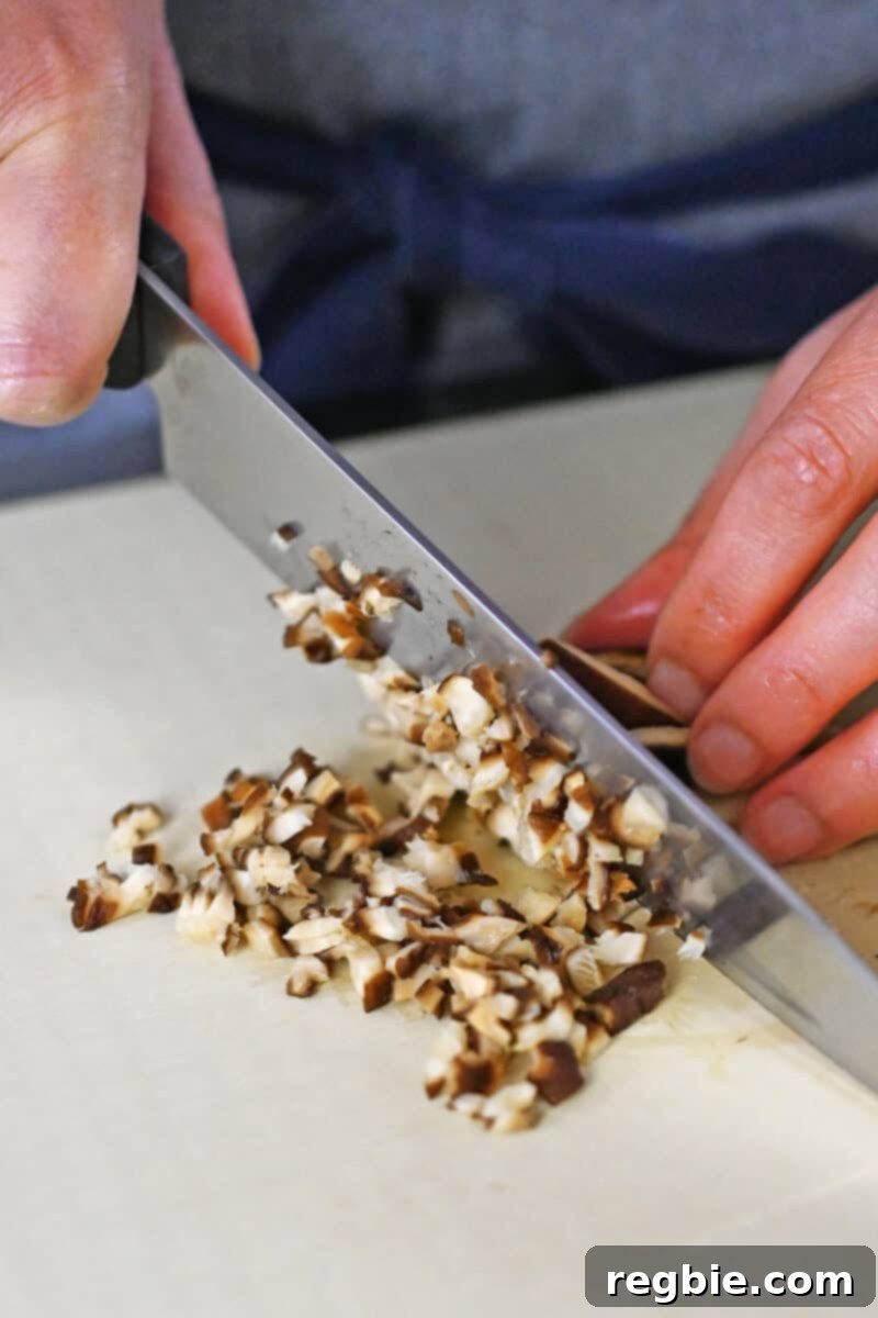 Closeup of someone finely chopping rehydrated dried shiitake mushrooms on a cutting board, ready for mixing.