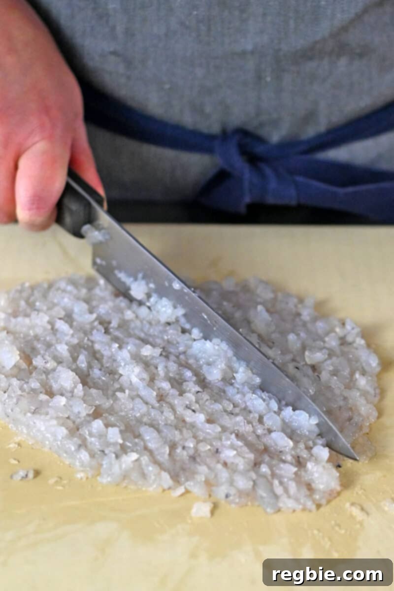 Raw shrimp is chopped into a fine paste on a cutting board with a chef's knife, showing proper consistency.