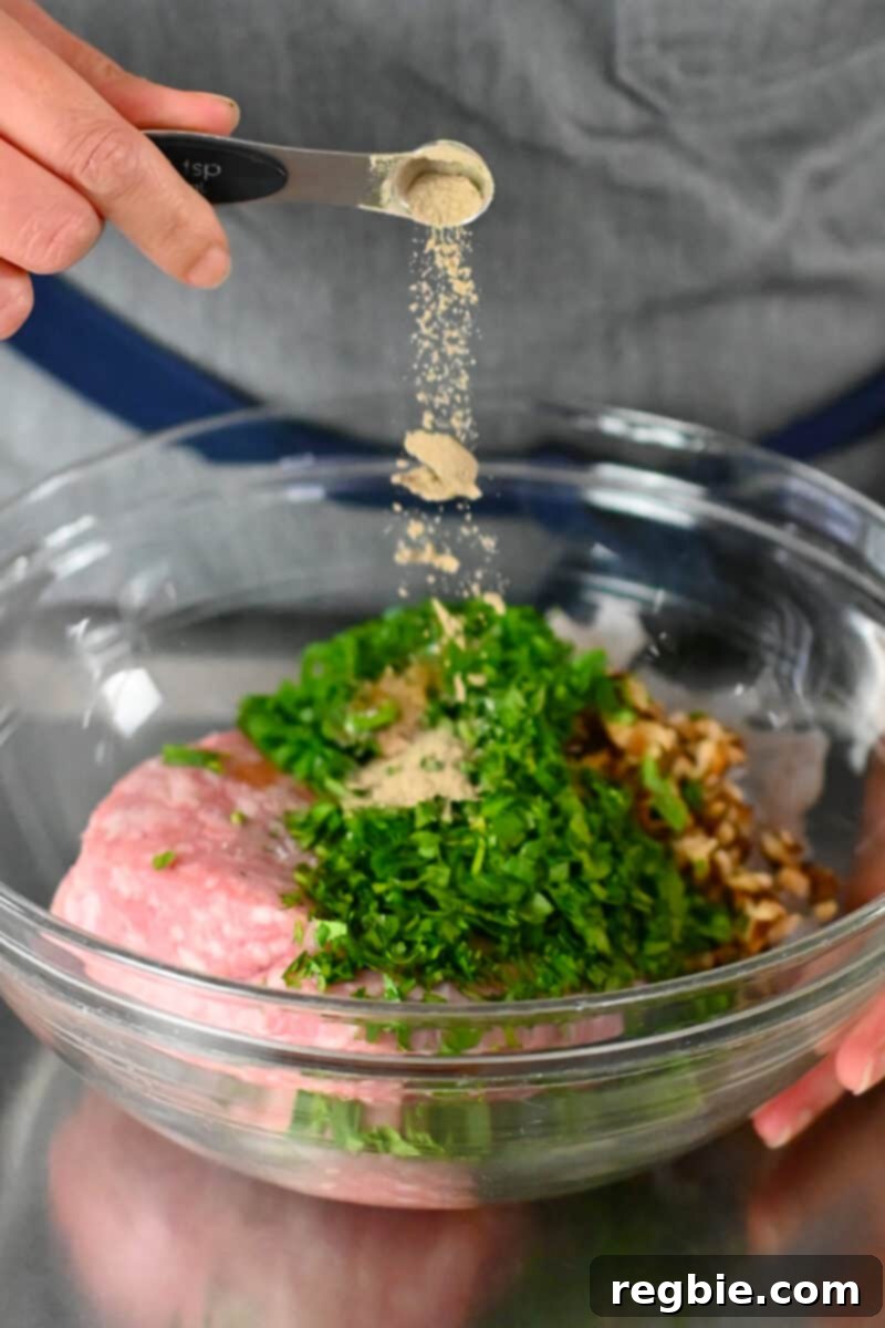 Adding a spoonful of white pepper to a bowl filled with all the ingredients for wonton meatballs.