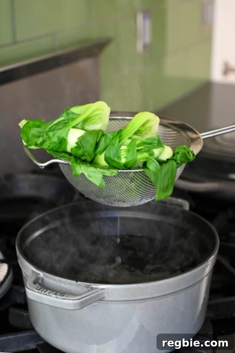 Removing some blanched baby bok choy from a pot of boiling water with a slotted spoon.
