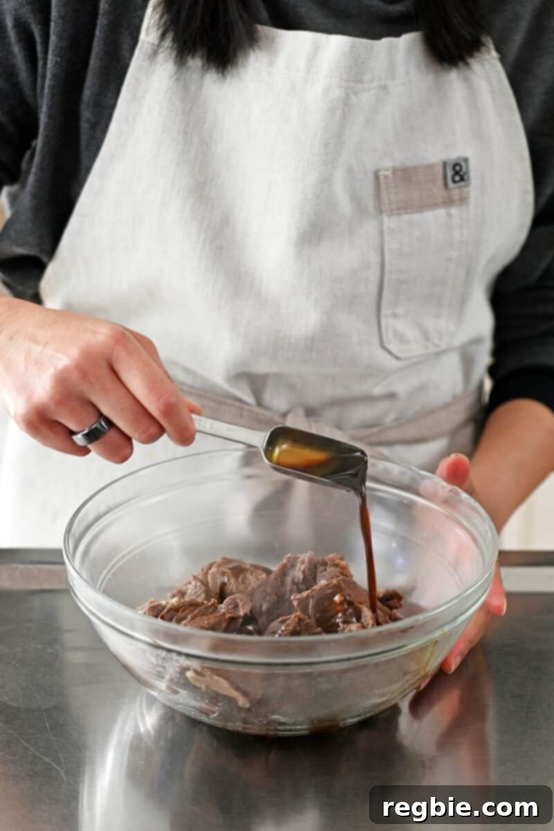 Adding a spoonful of coconut aminos to a bowl of stewed beef cubes, enhancing their flavor.