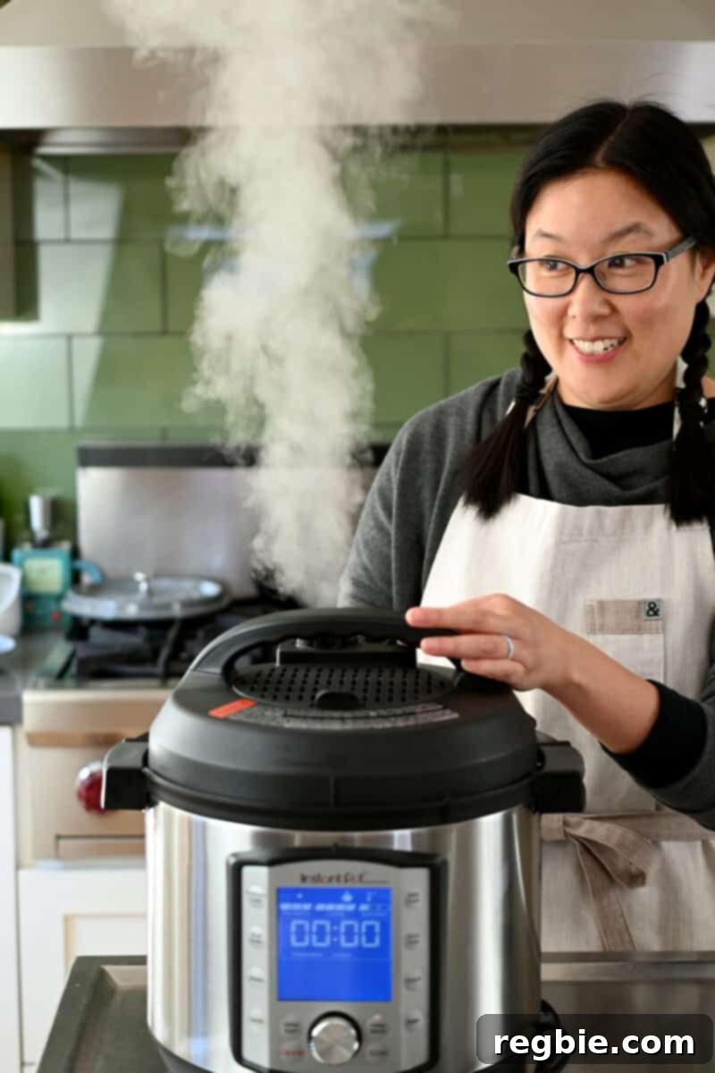 A smiling Asian woman is carefully depressurizing her Instant Pot, steam releasing from the valve.