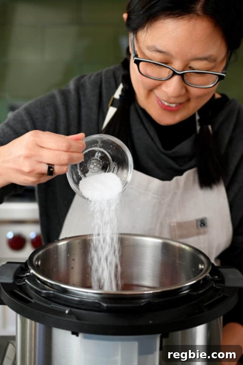 An Asian woman in glasses is adding salt to an open Instant Pot, carefully seasoning the Chinese Braised Beef Noodle Soup ingredients.