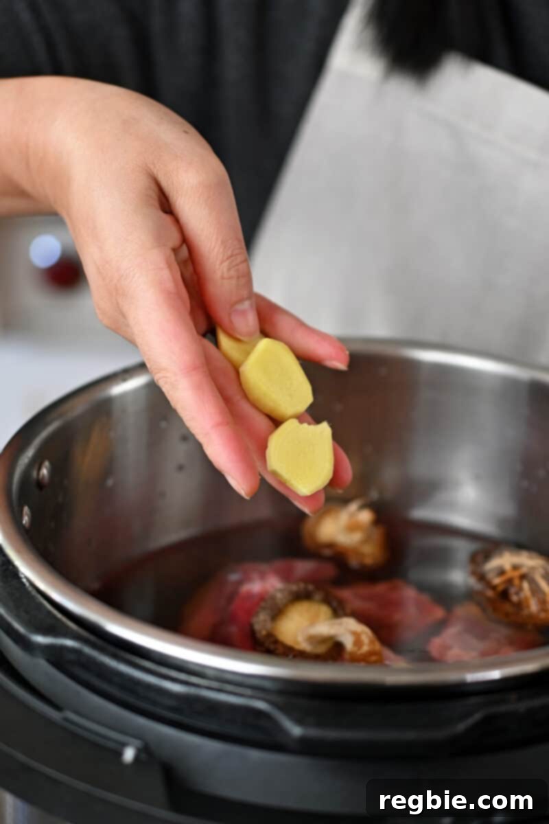 Adding thinly sliced fresh ginger to an open Instant Pot, which already contains other ingredients for Chinese Beef Noodle Soup.