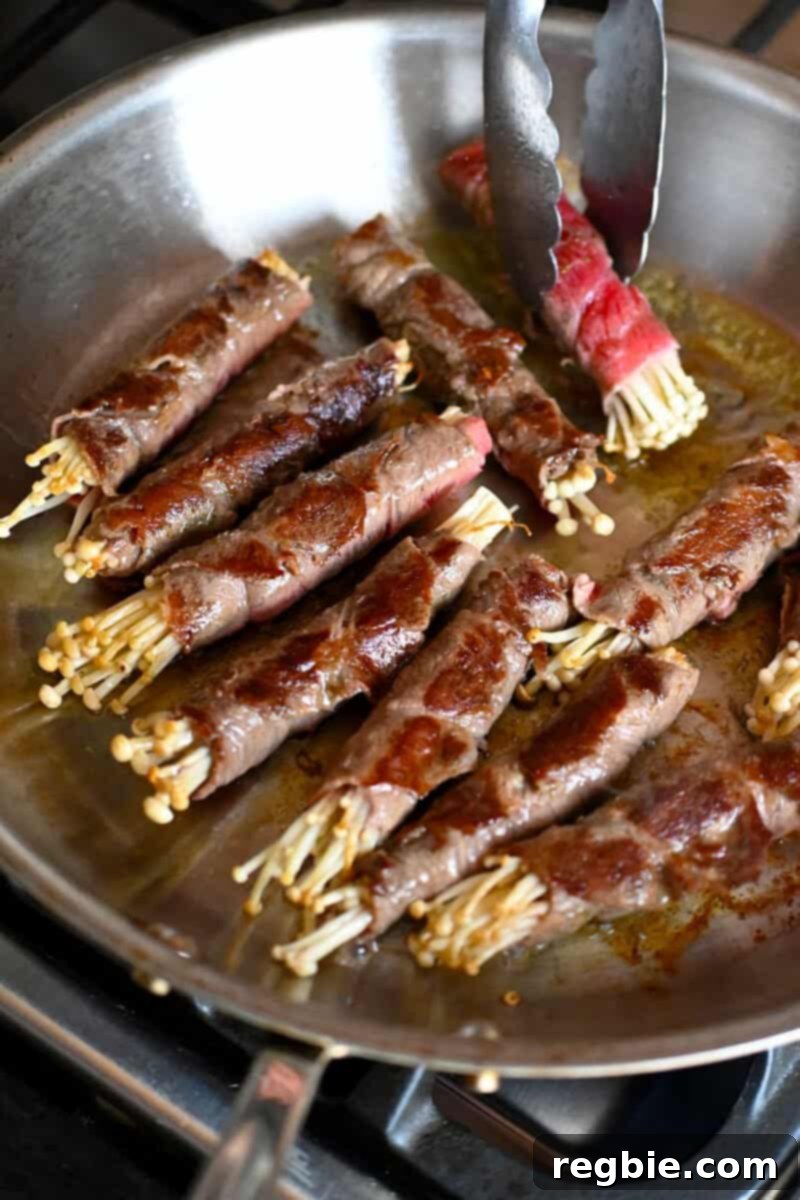 Wholesome Enoki Beef Wraps 13 Golden brown beef and enoki rolls frying in a large skillet, showing all sides evenly cooked.