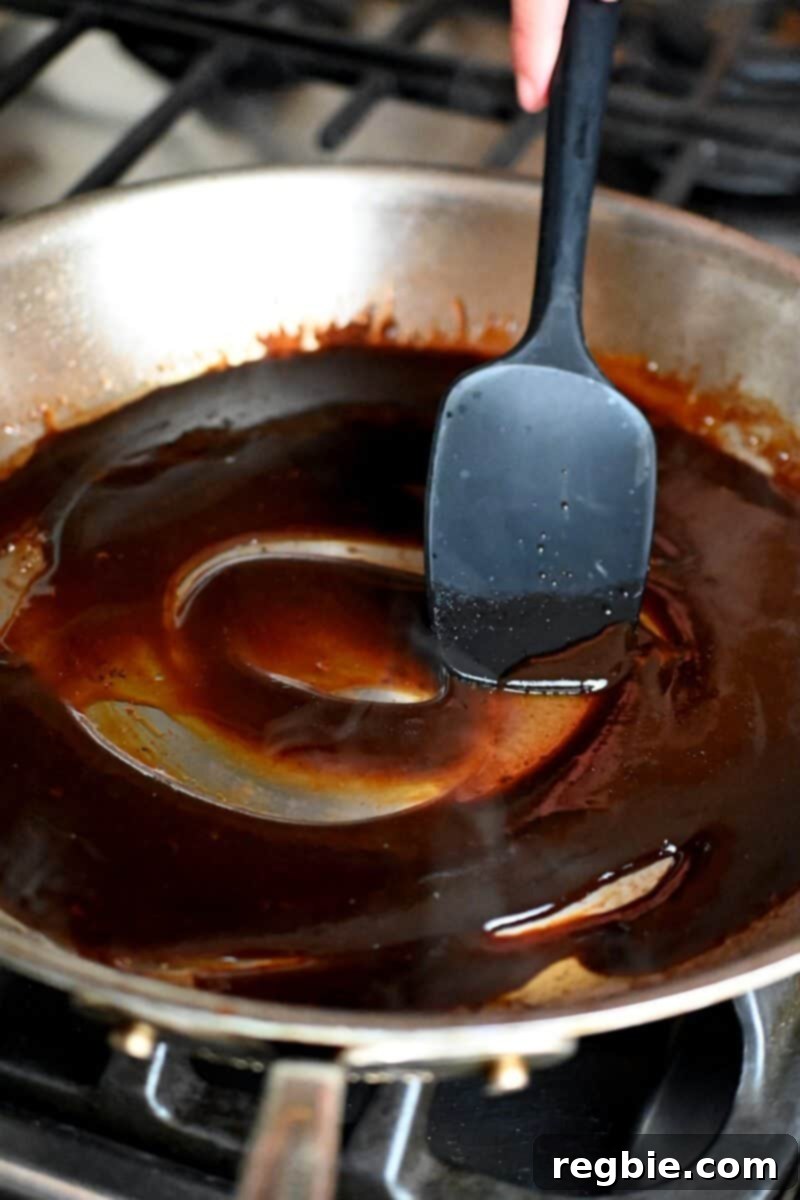 Wholesome Enoki Beef Wraps 17 A spatula is scraping through thickened sauce in a skillet, showing its reduced and glossy texture.