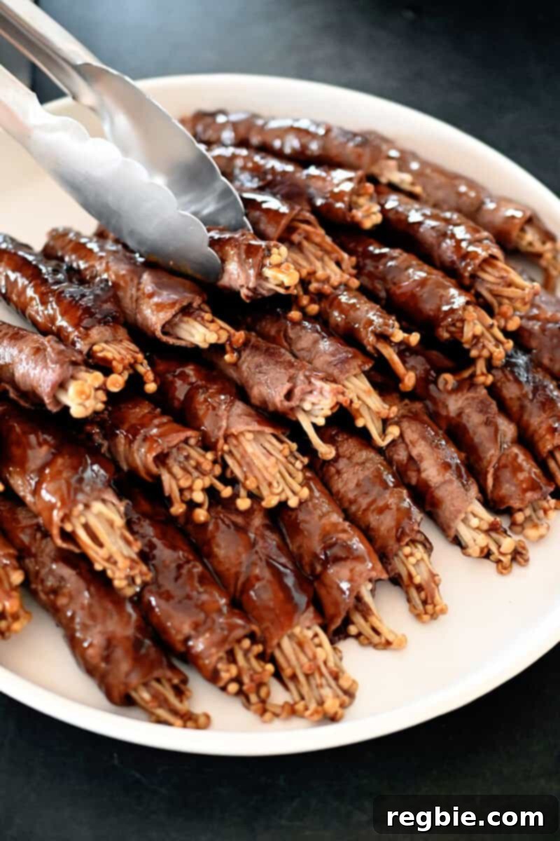 Wholesome Enoki Beef Wraps 19 A white plate filled with a large stack of cooked beef and enoki mushroom rolls, beautifully arranged.