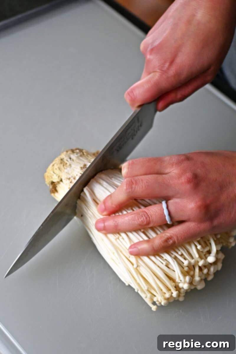 Wholesome Enoki Beef Wraps 5 A chef's knife is cutting the root ends off of a bunch of enoki mushrooms on a cutting board