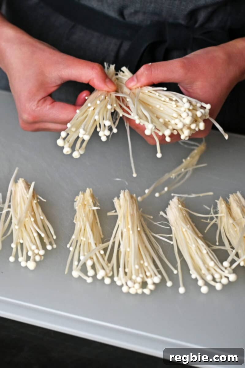 Wholesome Enoki Beef Wraps 6 A person is using their hands to carefully separate enoki mushrooms into small bundles.