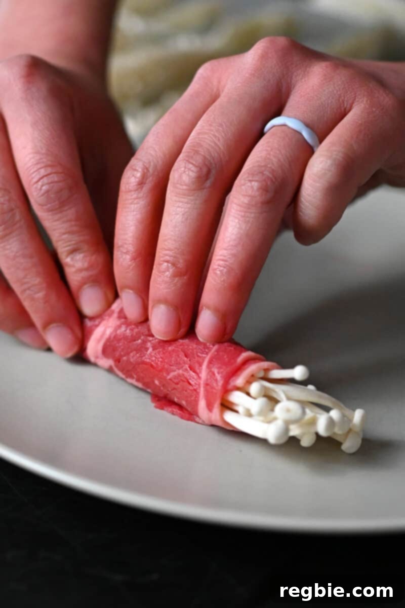 Wholesome Enoki Beef Wraps 8 Two hands are rolling enoki mushrooms in a thin slice of raw beef, demonstrating the wrapping technique.