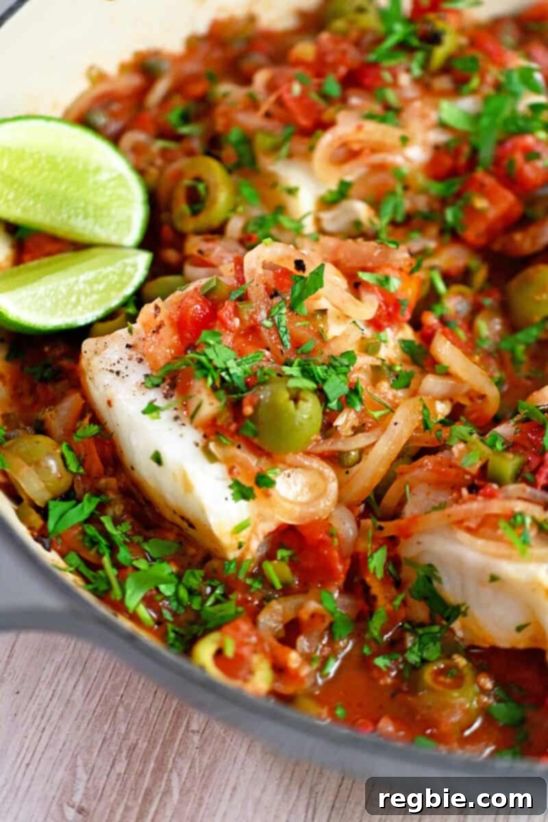 A close-up shot of tender white fish fillets in a zesty Veracruz sauce, beautifully presented in a skillet with bright lime wedges on the side, ready for serving.