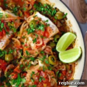 An overhead shot of white fish Veracruz in a skillet with sliced lime wedges on the side, ready to be served.