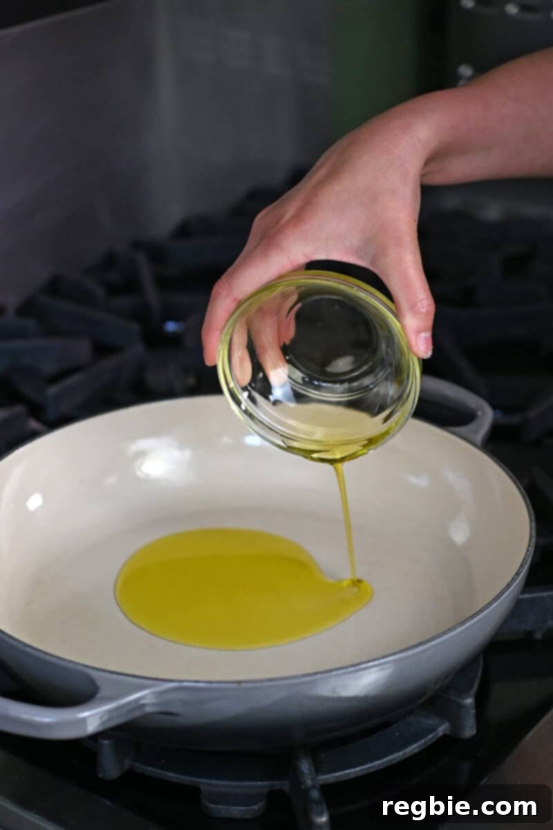A steady stream of golden olive oil is poured into a hot, large skillet, forming the essential base for the rich Veracruz sauce.