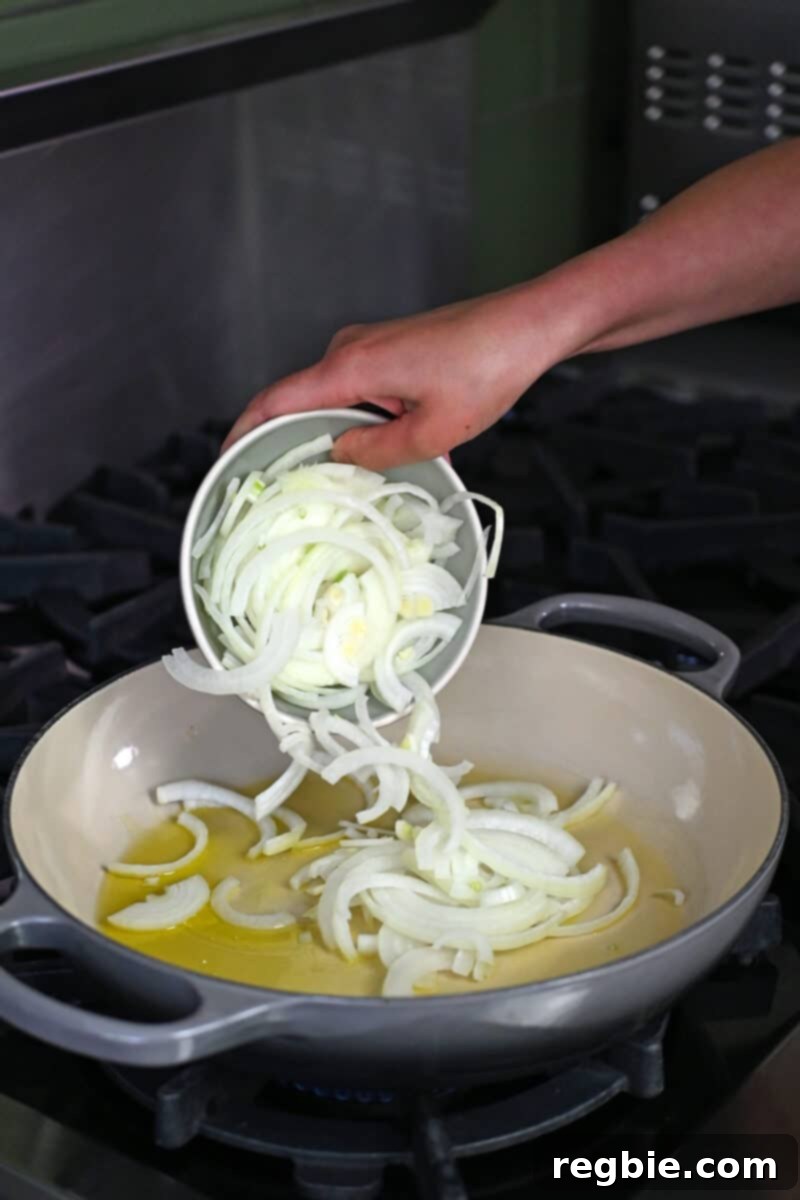 Thinly sliced yellow onions are added to a hot skillet filled with olive oil, ready to be sautéed until tender and translucent for the Veracruz sauce.