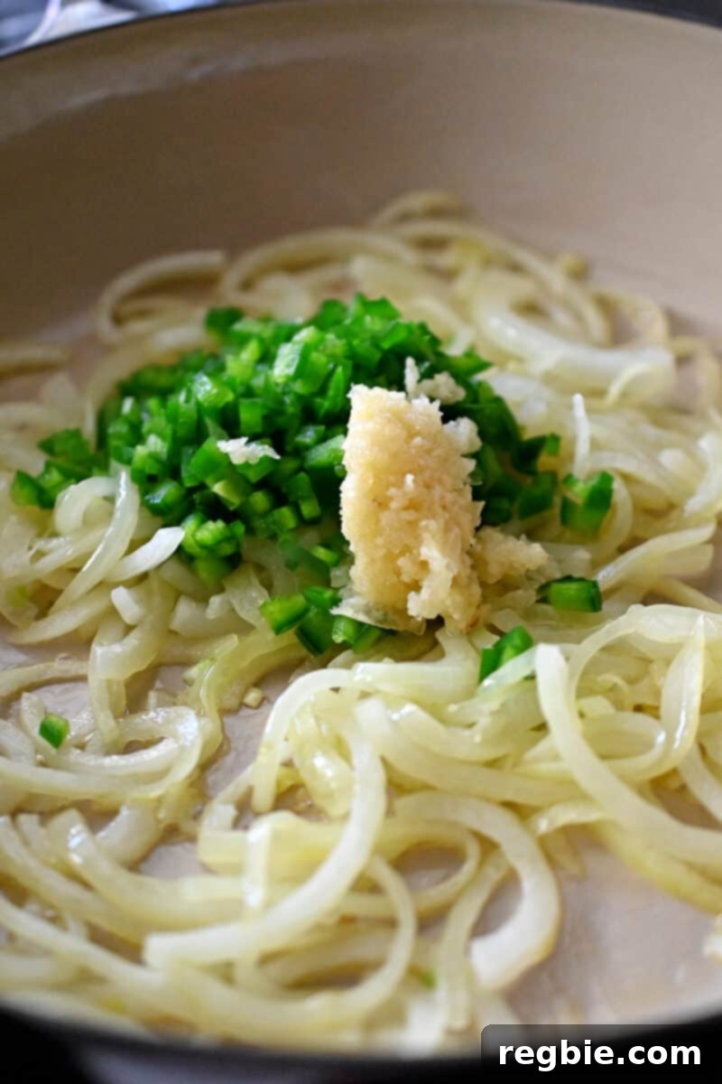 A close-up view of softened, translucent onions mixed with finely minced Anaheim peppers and garlic, releasing their aromatic flavors in the skillet.