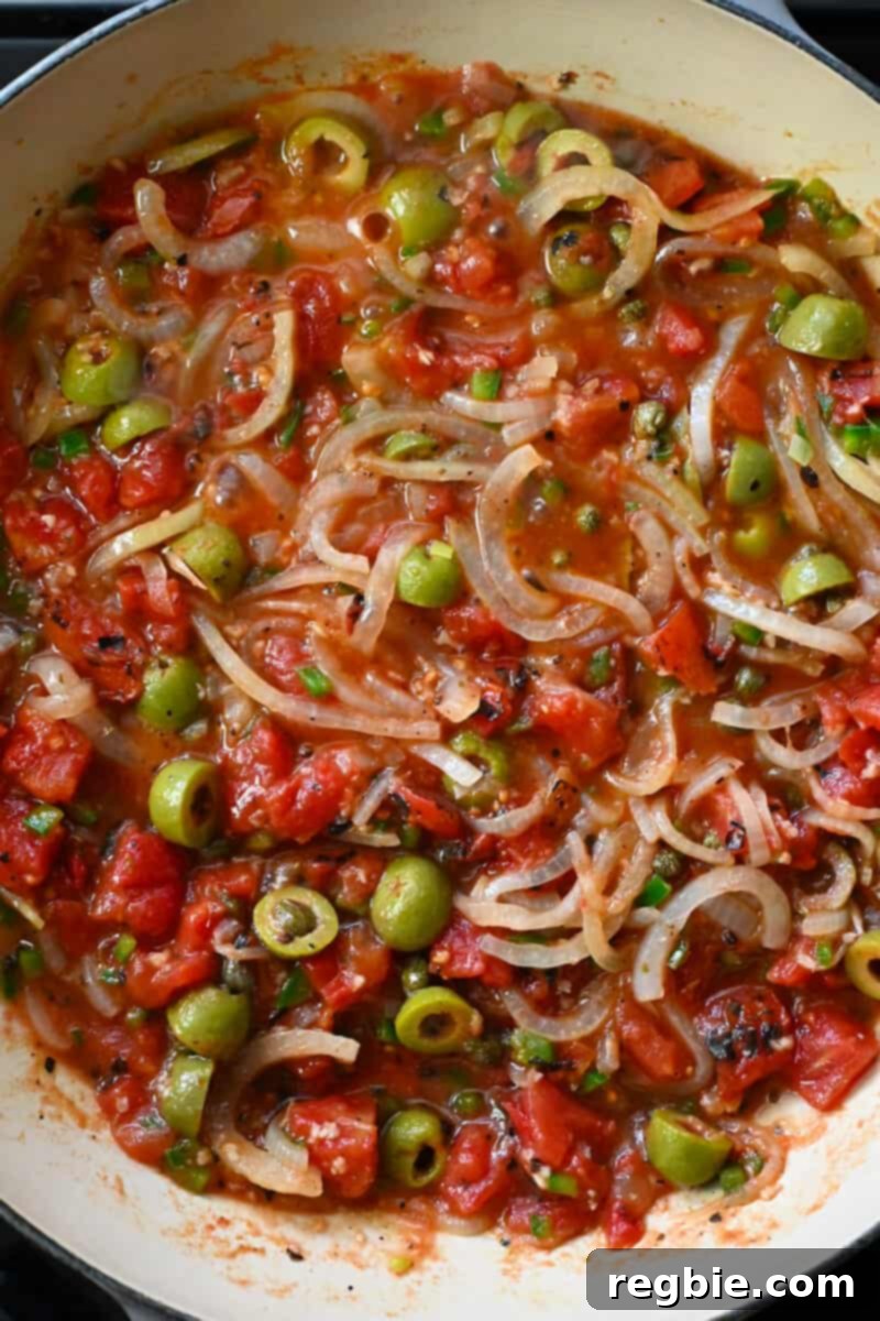An overhead view of a large skillet brimming with rich, reddish-orange Veracruz sauce, gently simmering as the flavors develop and intensify.