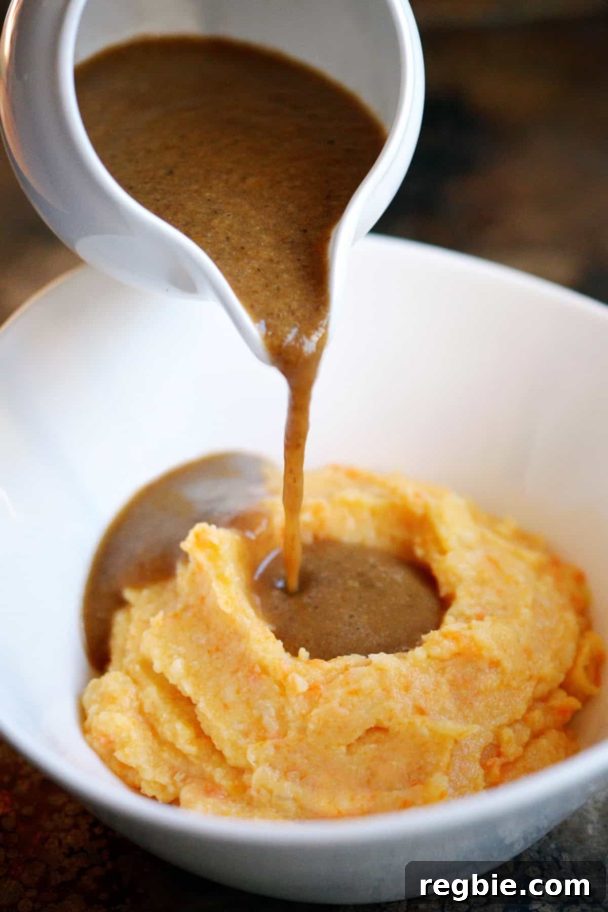 Pouring a gluten free gravy from a gravy boat onto a bowl filled with an orange root vegetable mash.