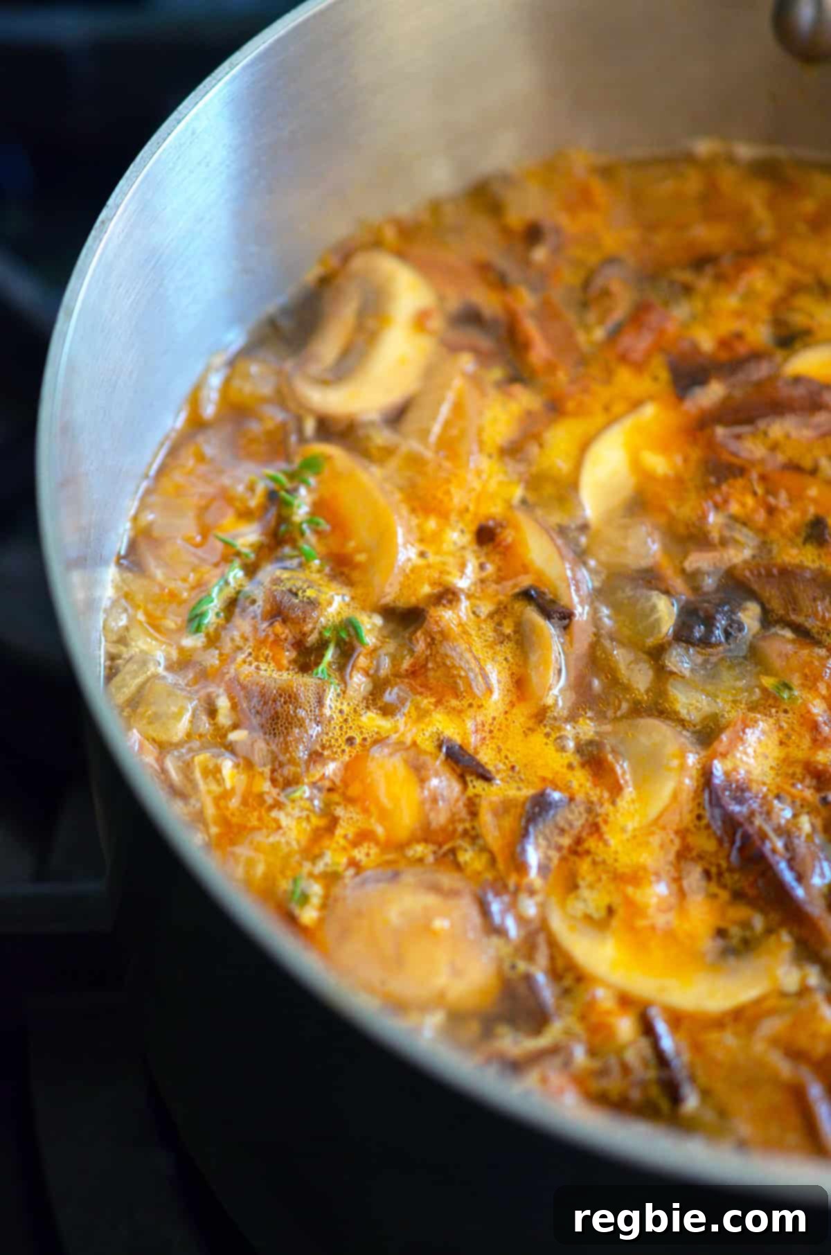A closeup of a saucepan filled with a simmering broth filled with sliced mushrooms, thyme, onions, and broth to make umami gravy.