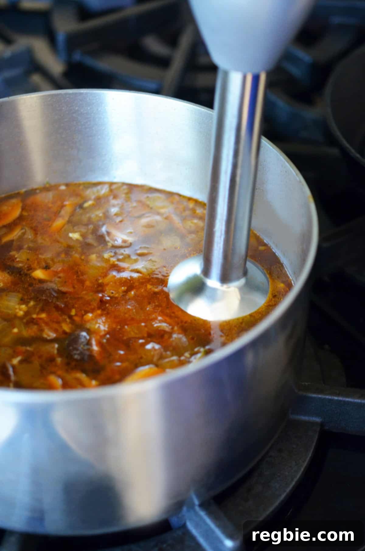 An immersion blender is blending a gluten free gravy with lots of umami in a small saucepan.